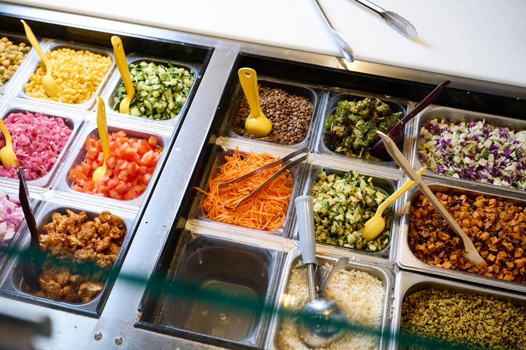  Individual metal containers of fresh ingredients, scoops, and tongs at Forage Kitchen.