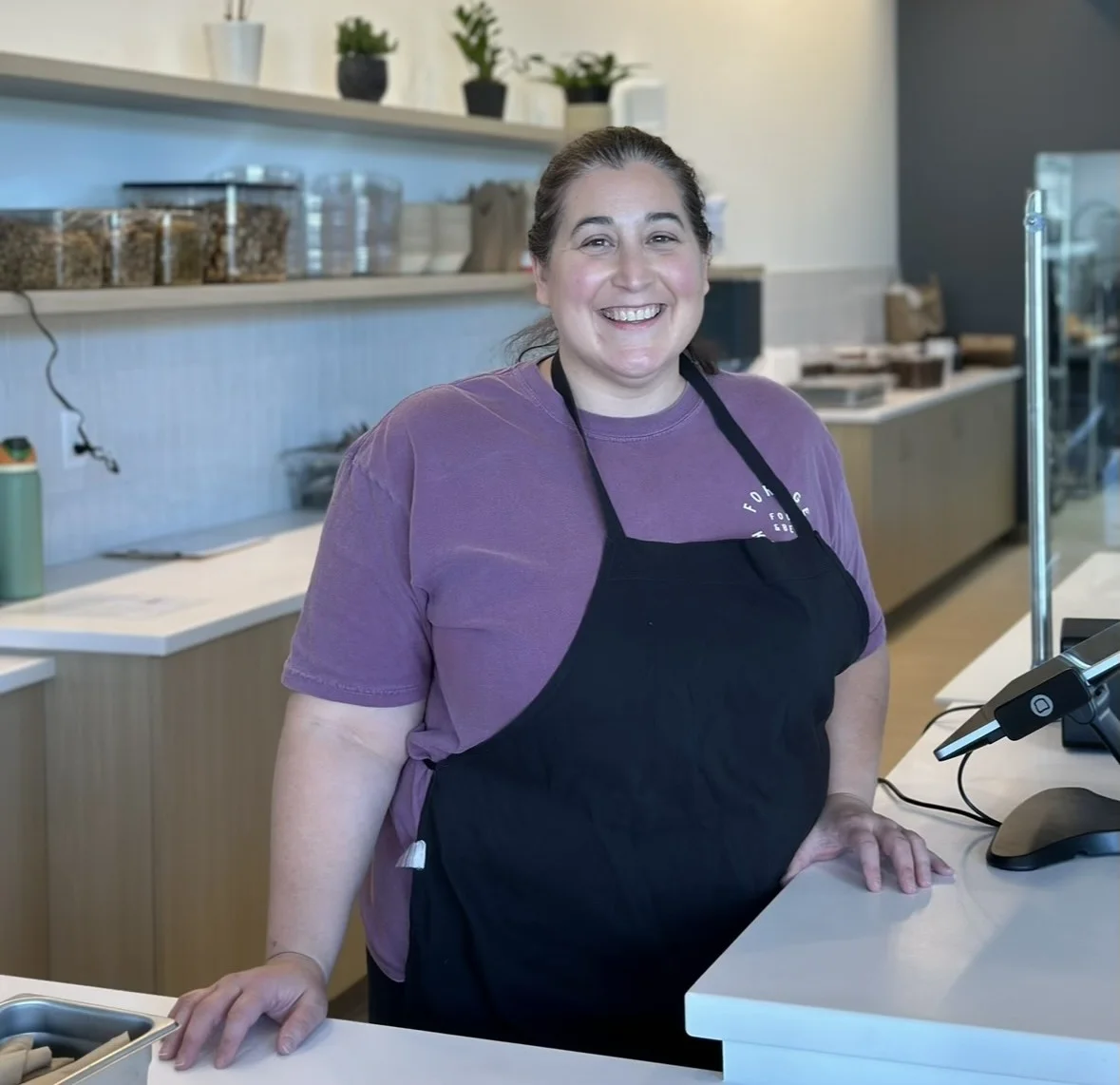  A smiling Forage Kitchen staff member standing at the checkout register counter.