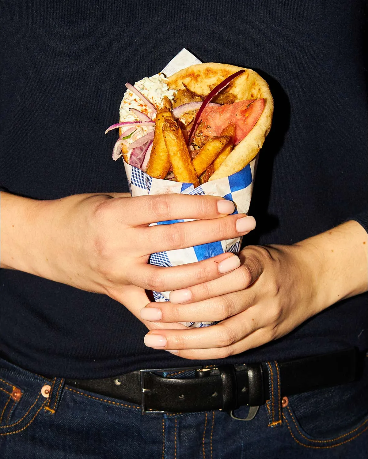 Hands holding a gyro wrap stuffed with fries, tomato, red onion and tzatziki