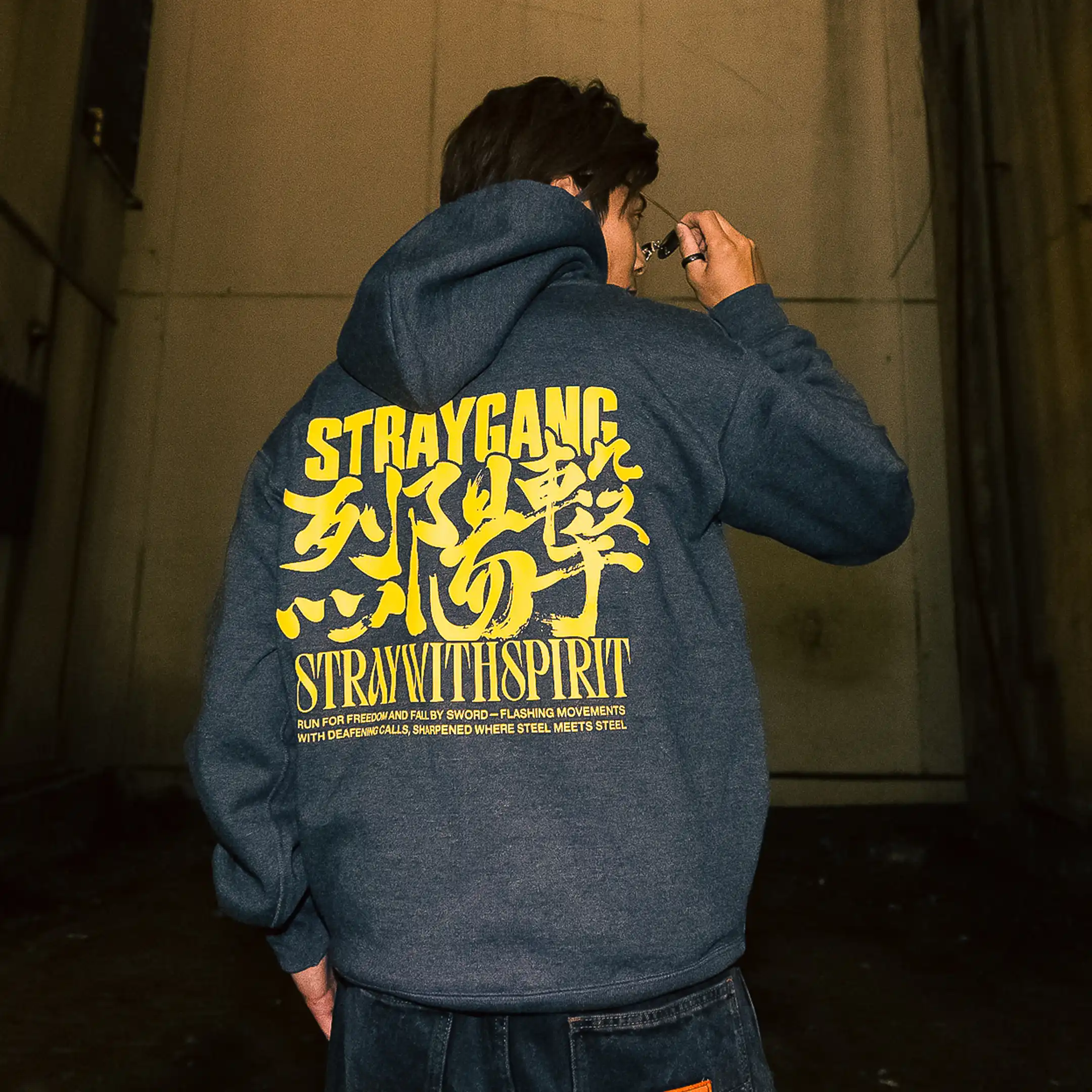 Campaign image highlighting the back screen print of Straygang's strike hoodie, worn in a dirty, Japanese abandoned alley.
