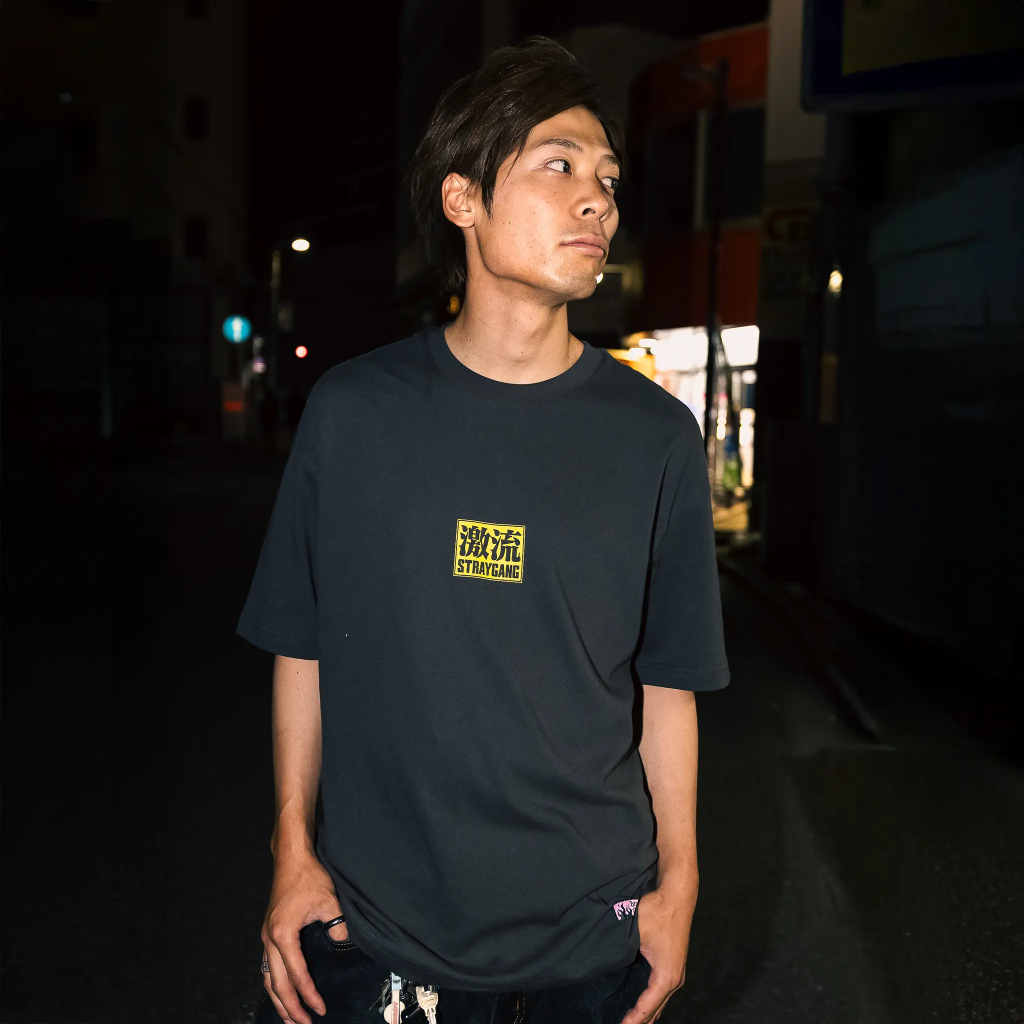 Campaign image of a skater wearing Straygang's grey supernova tee on the streets of Tokyo. The front design, says 'Straygang' with some Japanese kanji, adding some contrast to the backdrop. 