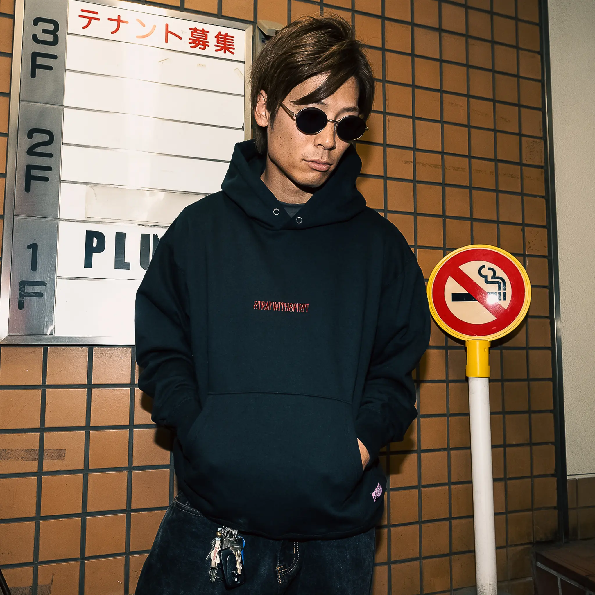 Campaign image highlighting the front embroidered design of Straygang's strike hoodie, worn in a Tokyo alley.