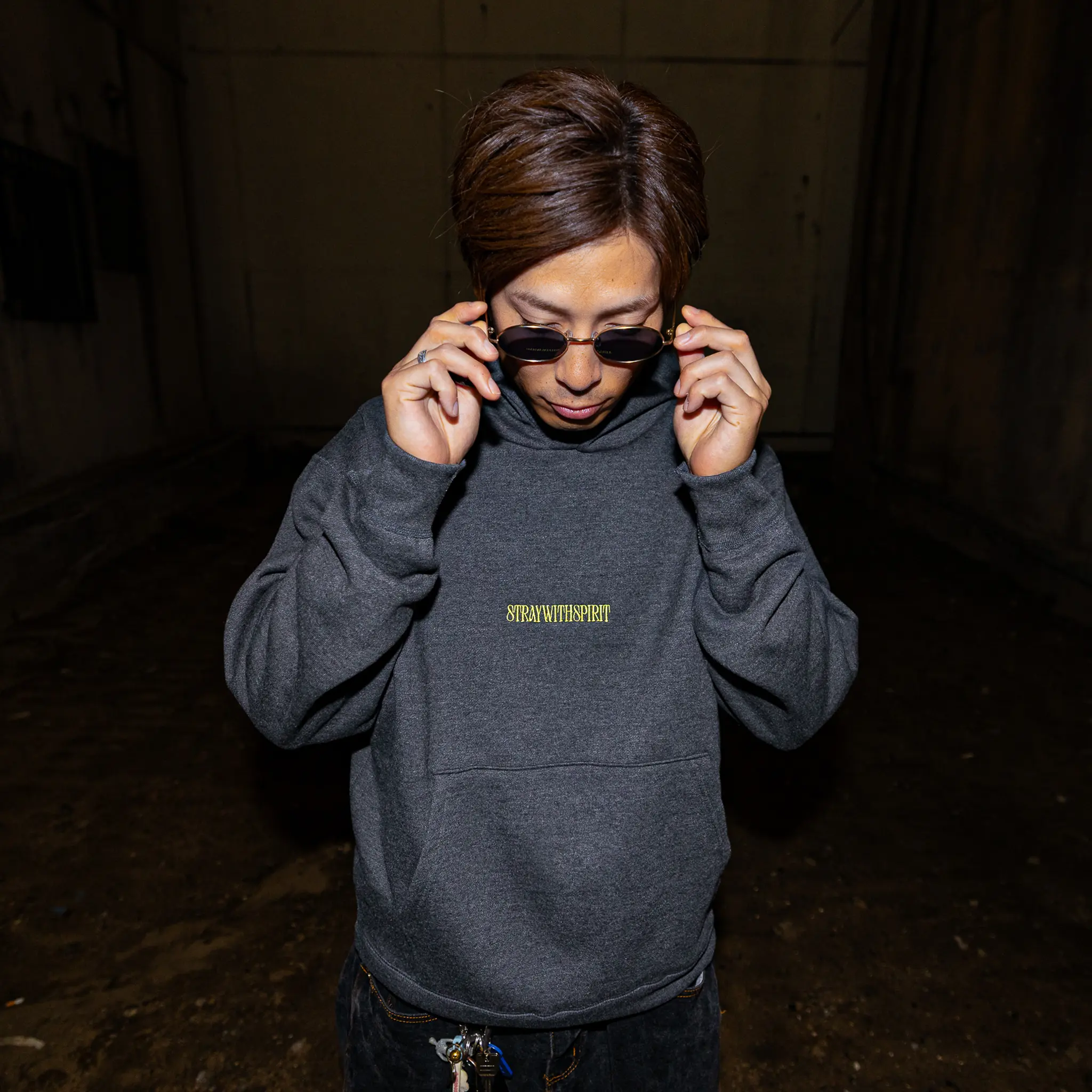 Campaign image of a skater wearing Straygang's grey strike hoodie in the dark streets of Japan. The front design, a small, high quality embroidery reading "stray with spirit".