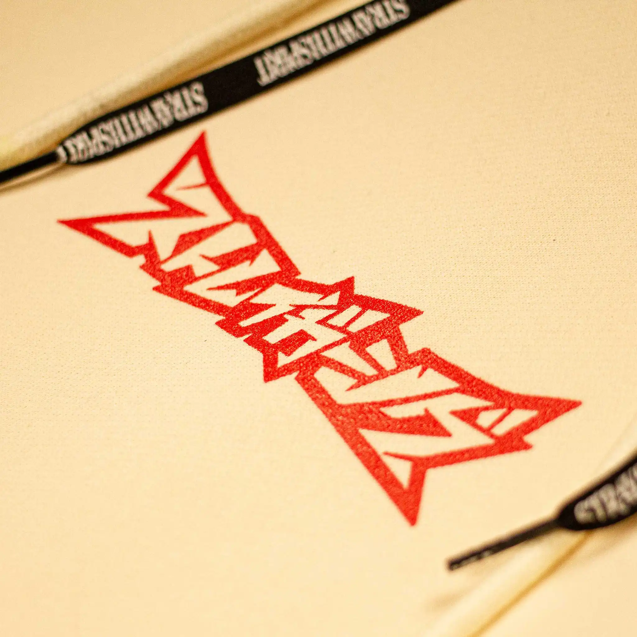 Straygang Spirit Hoodie in cream, chest detail of sharp red Straygang logo print with branded drawstrings.