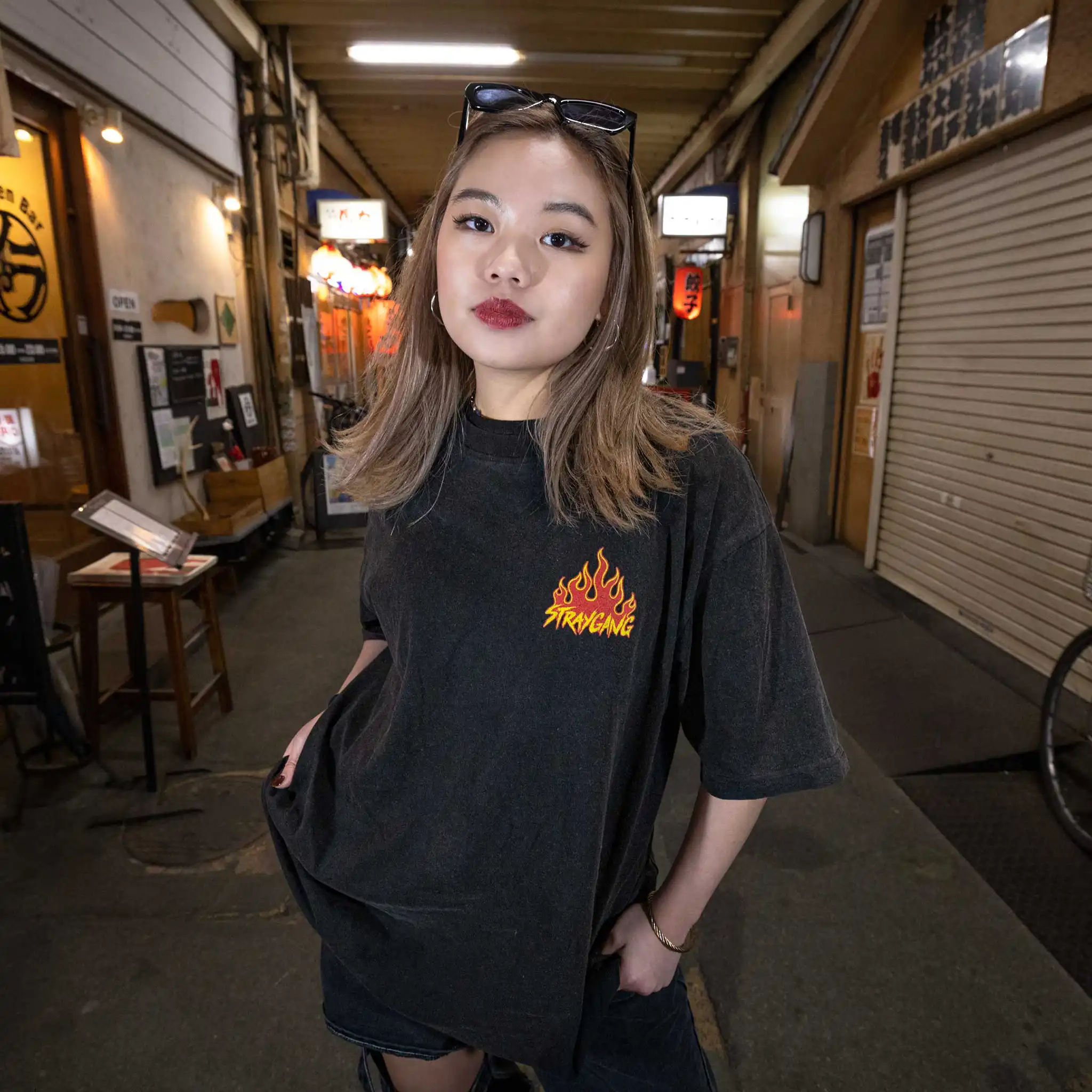 Model in a Tokyo alley wearing Straygang Racing Tee in black wash, front view, showing flame chest logo graphic.