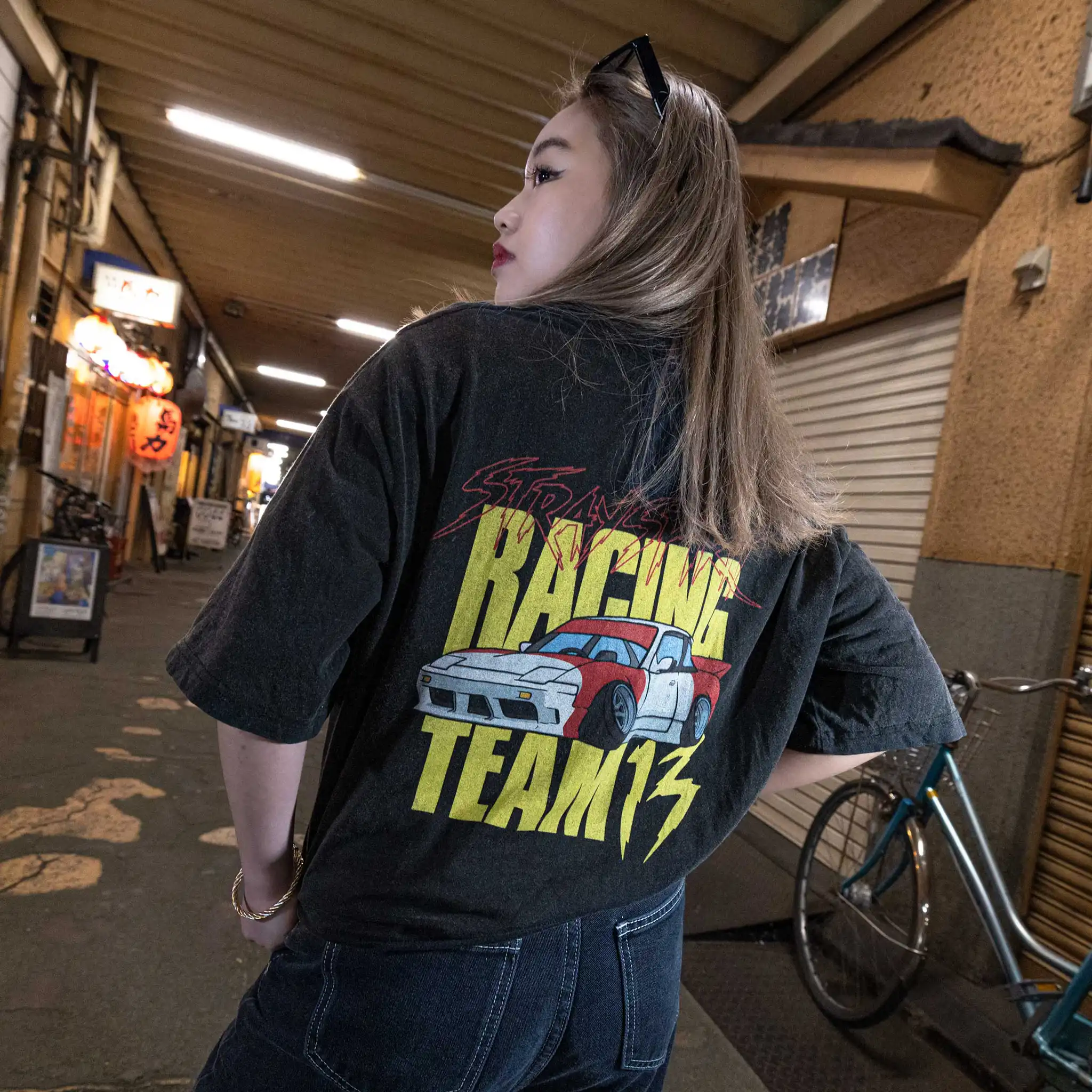 Model wearing Straygang Racing Tee in black wash, back view, with oversized “Racing Team 13” drift car graphic, shot in Tokyo alley.