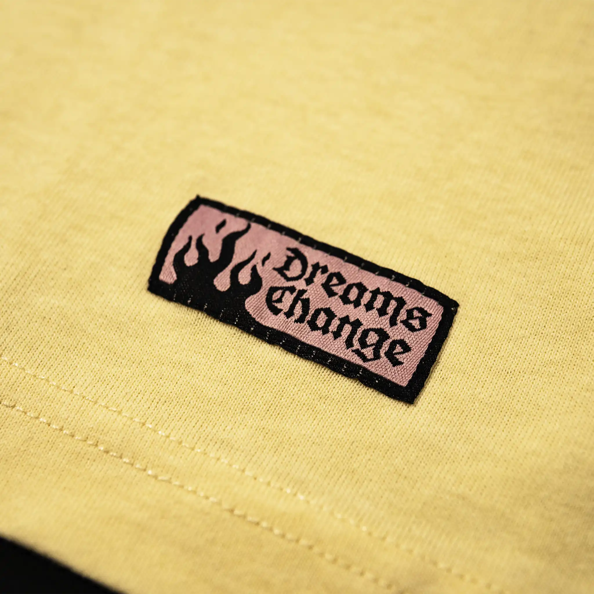 Woven label detail on Straygang Supernova Tee hem, pink ‘Dreams Change’ patch with flame graphic.
