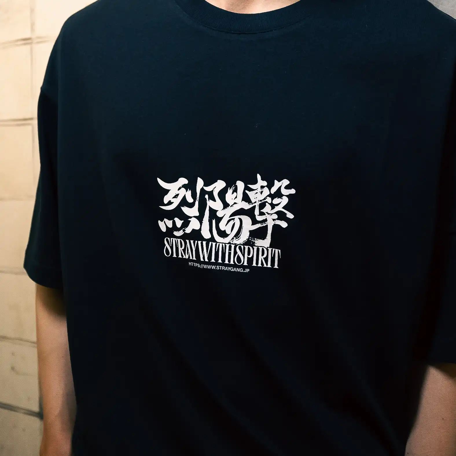 Lifestyle photo of Straygang Strike Tee in black, model wearing the graphic tee in a Tokyo back alley.