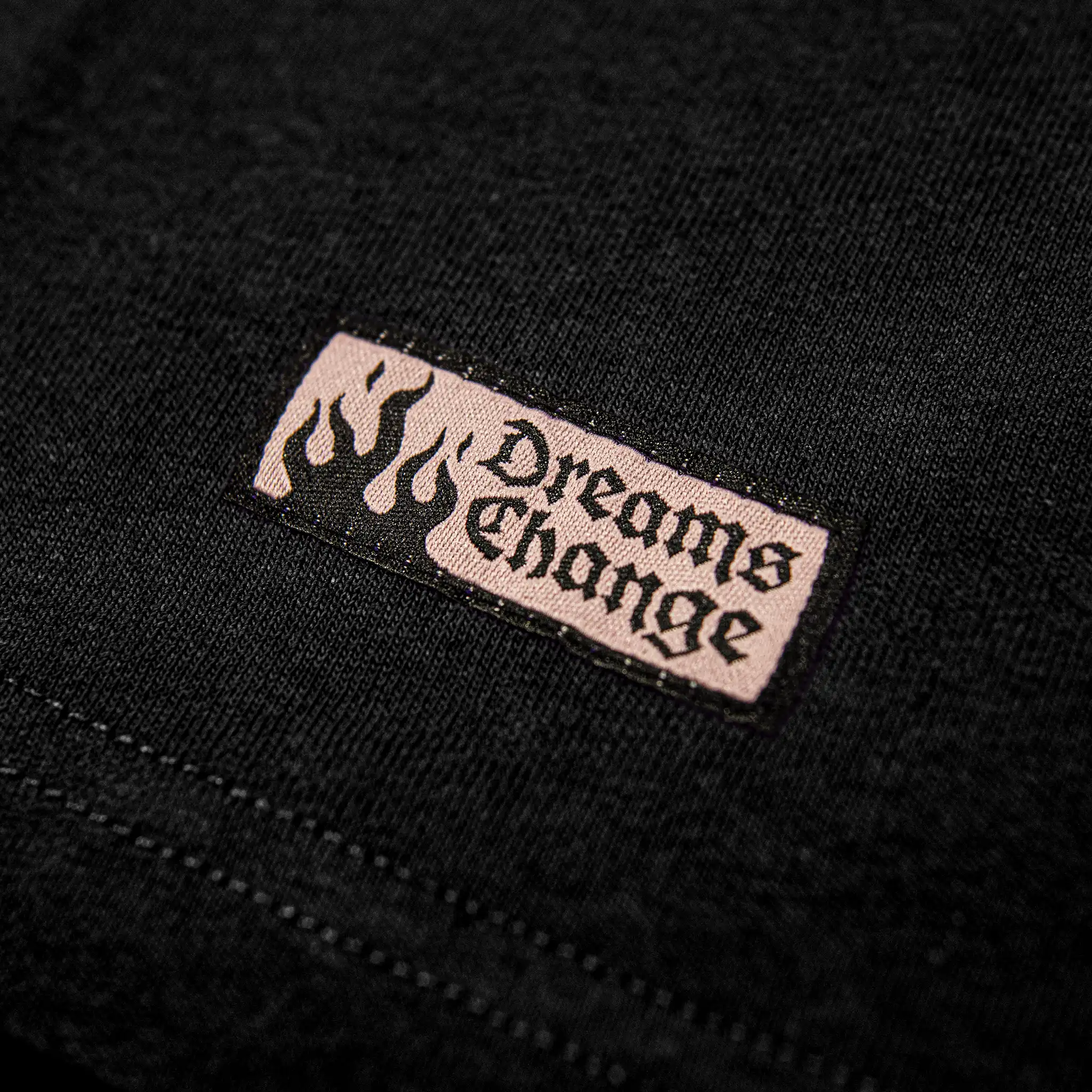 Woven hem patch on Straygang Strike Tee in black, flame design with ‘Dreams Change’ text.