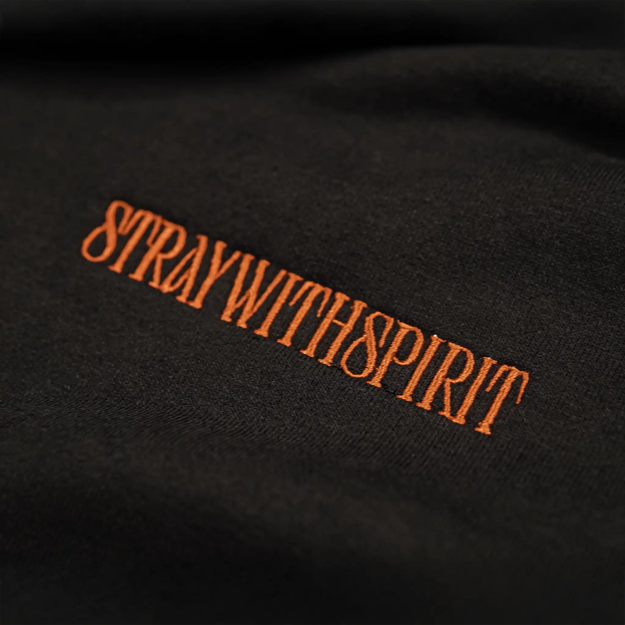 Close-up of the ‘Stray With Spirit’ embroidery on the Straygang Strike Hoodie in black, showing the textured threadwork and premium cotton weave.