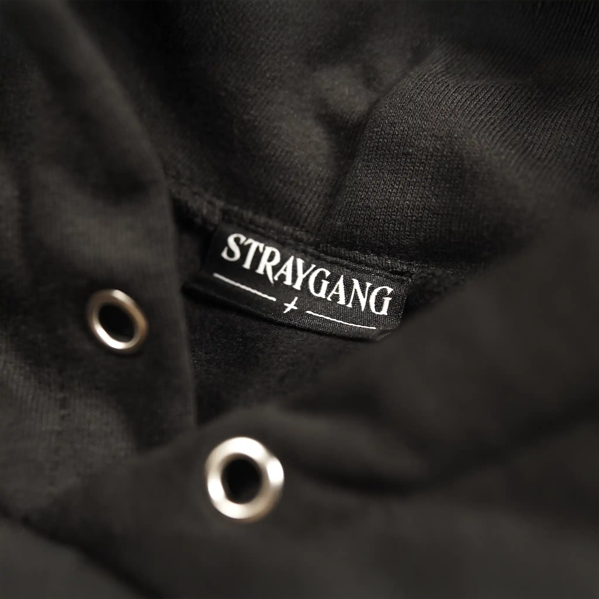 Neck label on the Straygang Strike Hoodie in black, featuring STRAYGANG woven branding tag stitched with metallic eyelets.