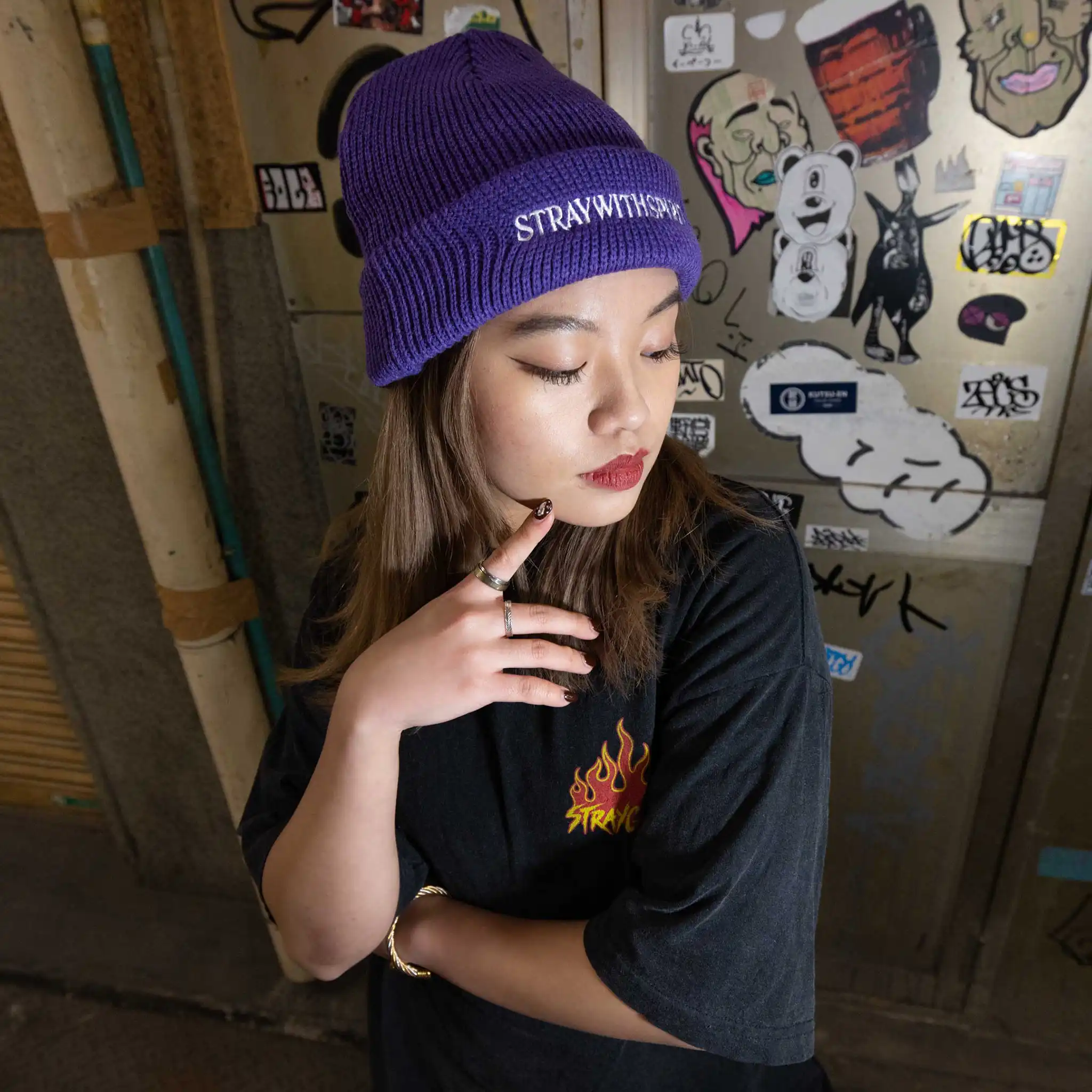 Campaign image of a model wearing Straygang's 'SWS' purple beanie in the filthy streets of Tokyo. The front design, and purple coloring stands out amidst the backdrop.