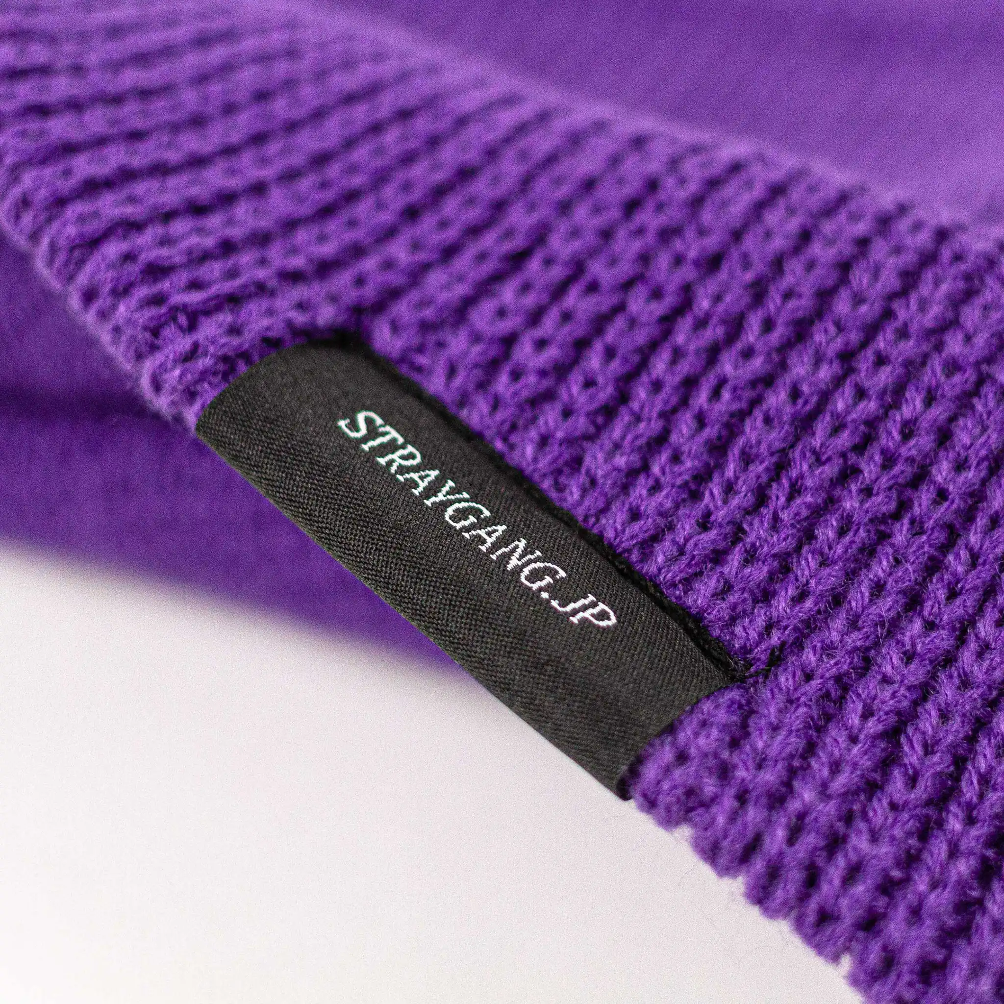 Close-up image highlighting the back of Straygang's 'SWS' purple beanie, showing the branded woven label in detail. This shot focuses on the inside of the label that has 'Straygang.jp' written on it,