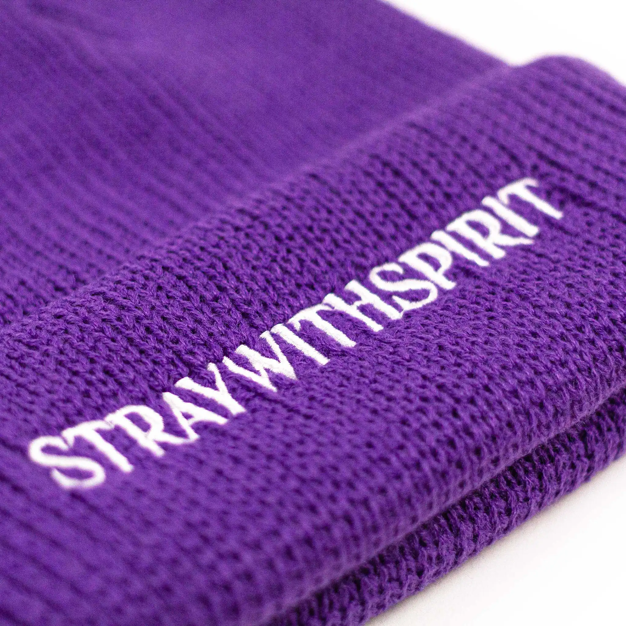 Close-up image highlighting the front of Straygang's 'SWS' purple beanie, showing the detailed embroidered lettering. The shot is a close-up of the lettering which says 'STRAYWITHSPIRIT' in serif typography.