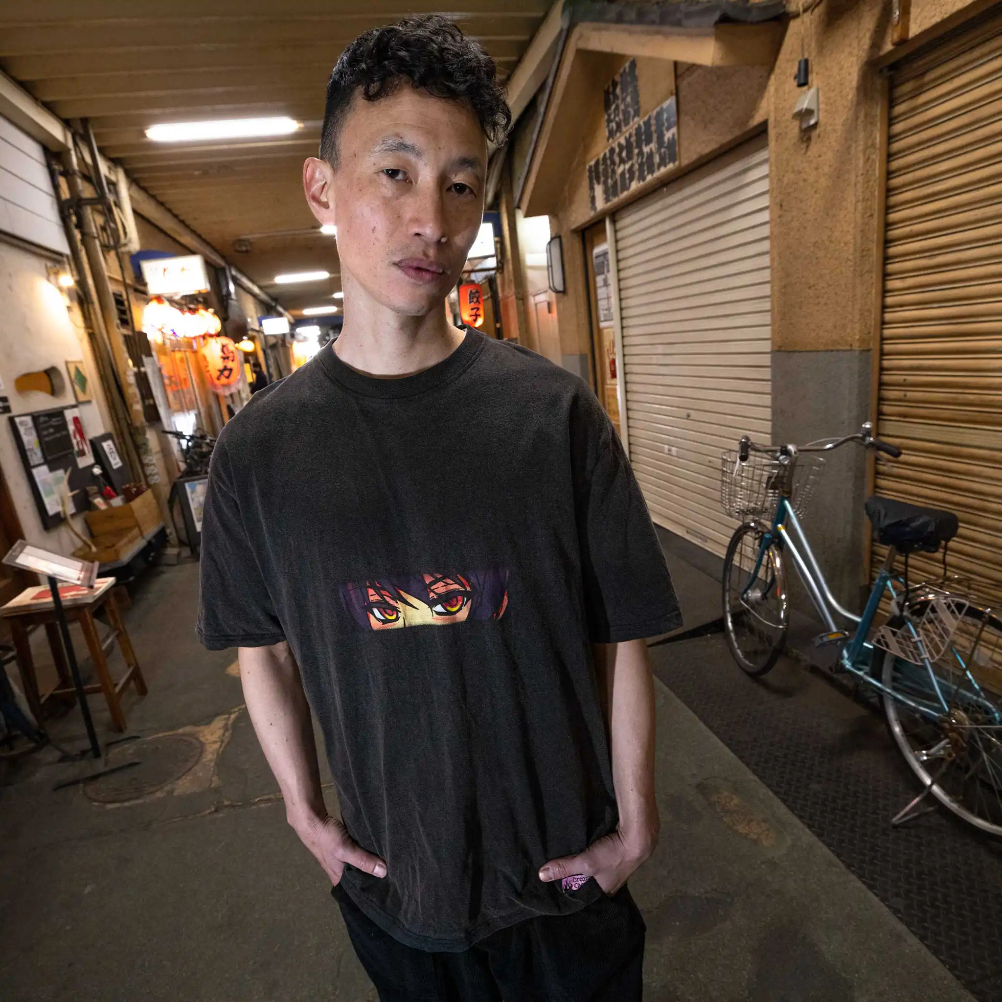 Campaign image that exhibits the front design of Straygang's black wash t-shirt, modeled amidst Tokyo's back-alleys. The digital print, draws attention away from the surroundings and to the tee's unique anime styled design.