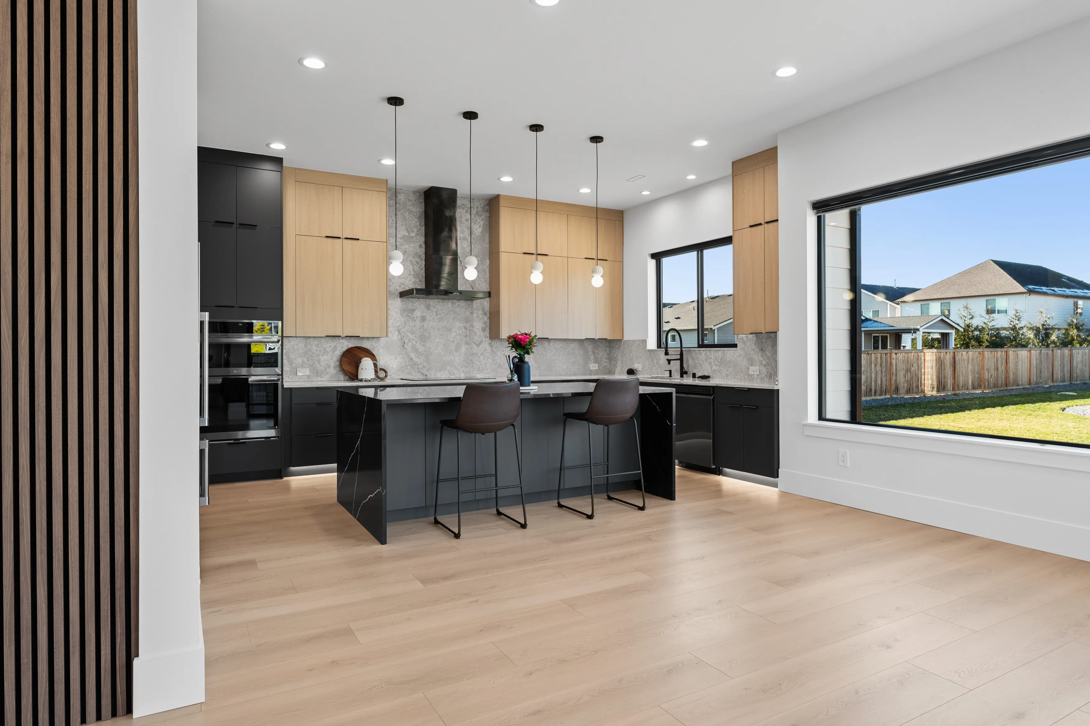 Fully custom modern kitchen in Issaquah with black and wood cabinetry, large island, pendant lighting, and open layout.