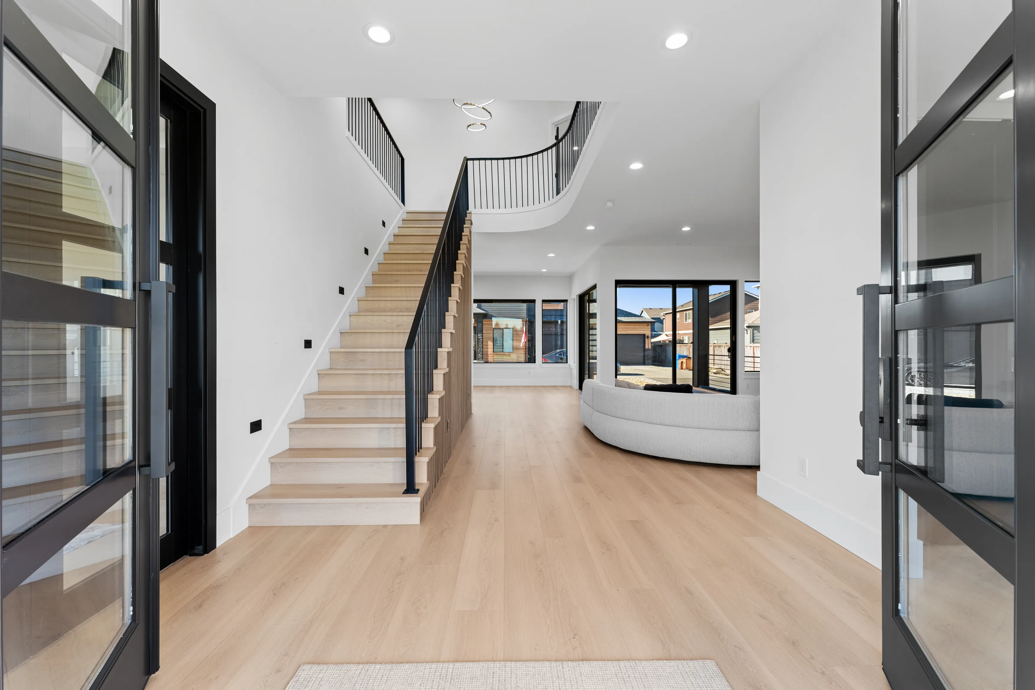Modern custom home interior in Issaquah featuring light wood flooring, open staircase with black railing, and a bright open-concept living space.