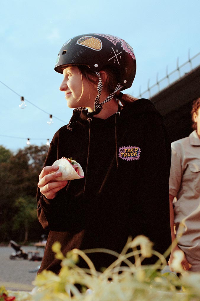 Person i svart hoodie med El Taco Trucks logotype som står och äter taco