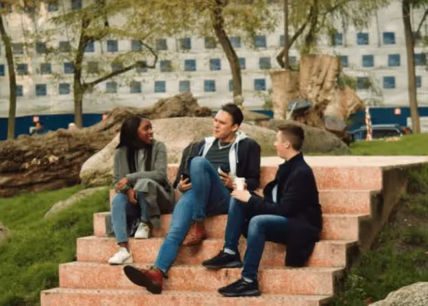 Students talking as they sit on steps in a park. 