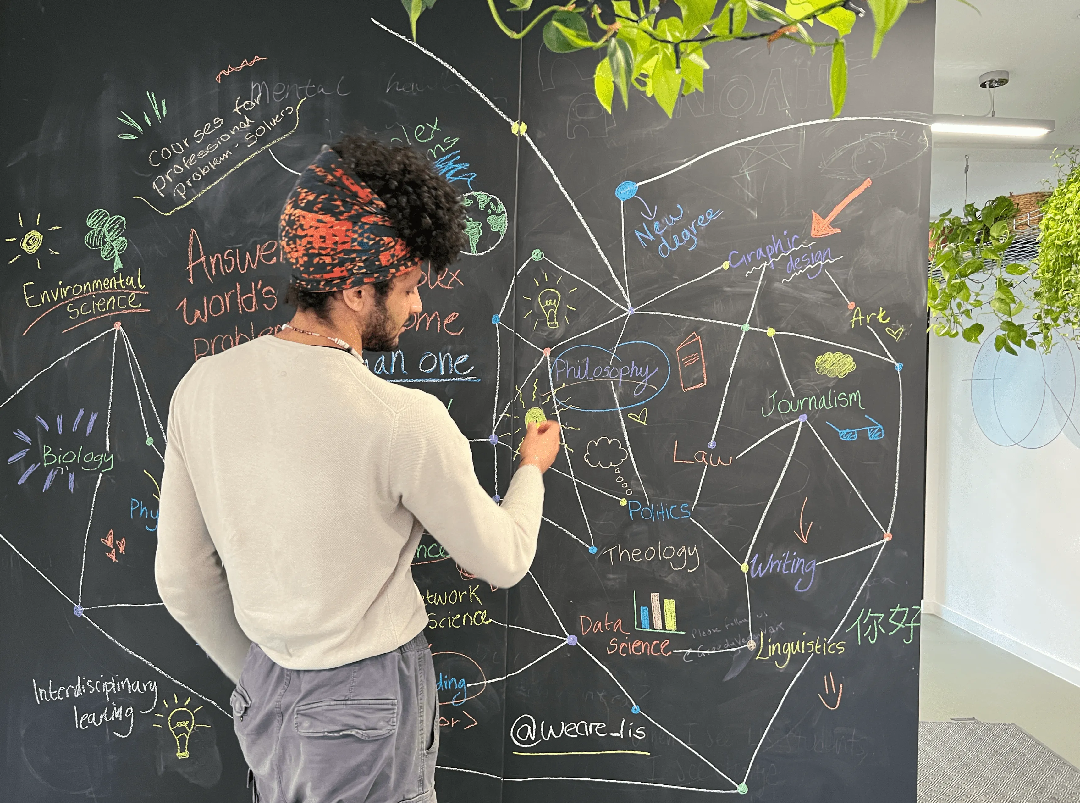 man with curly hair writing on a chalk board