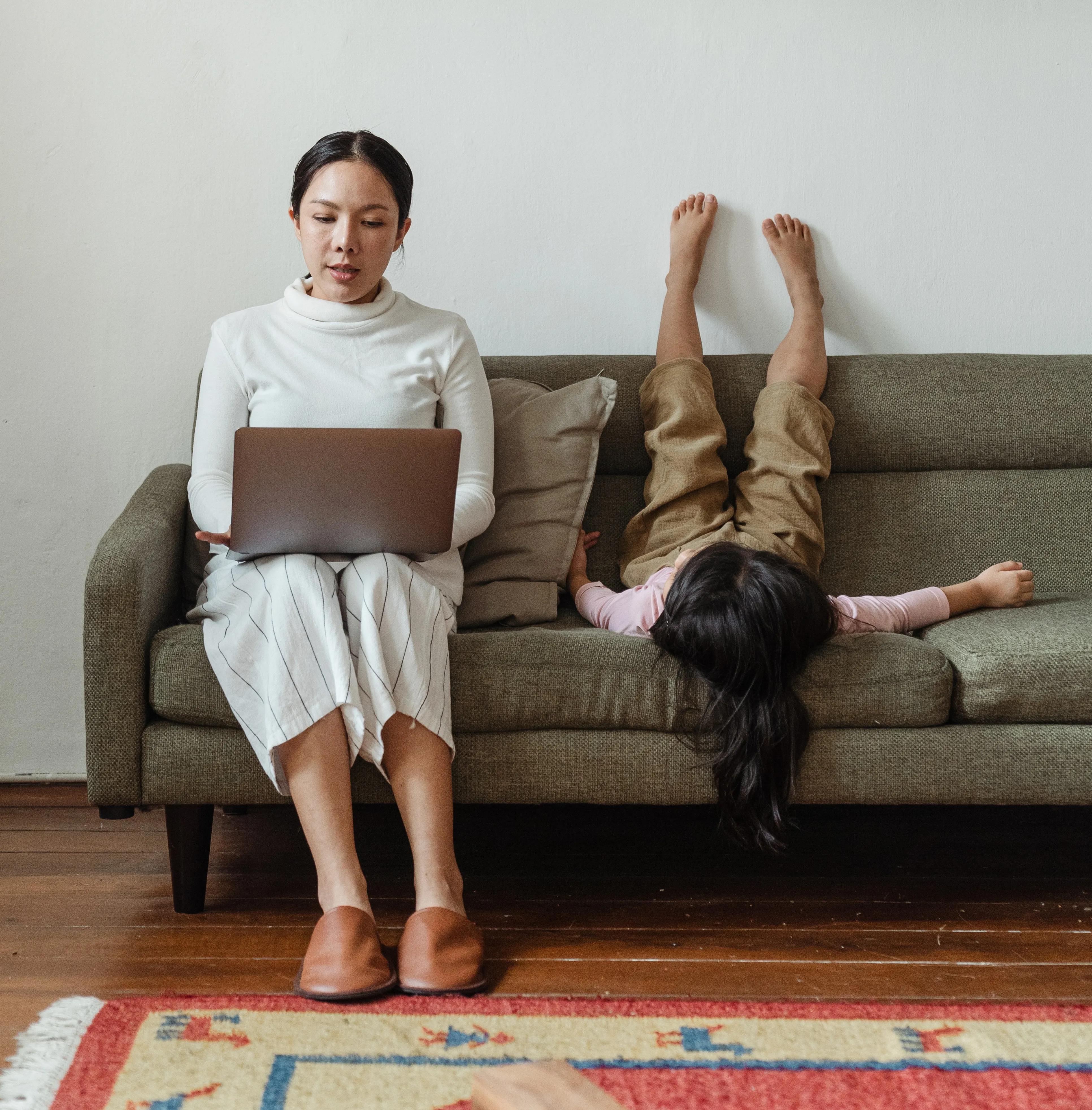 A mother is working from her laptop while her daughter plays next to her.