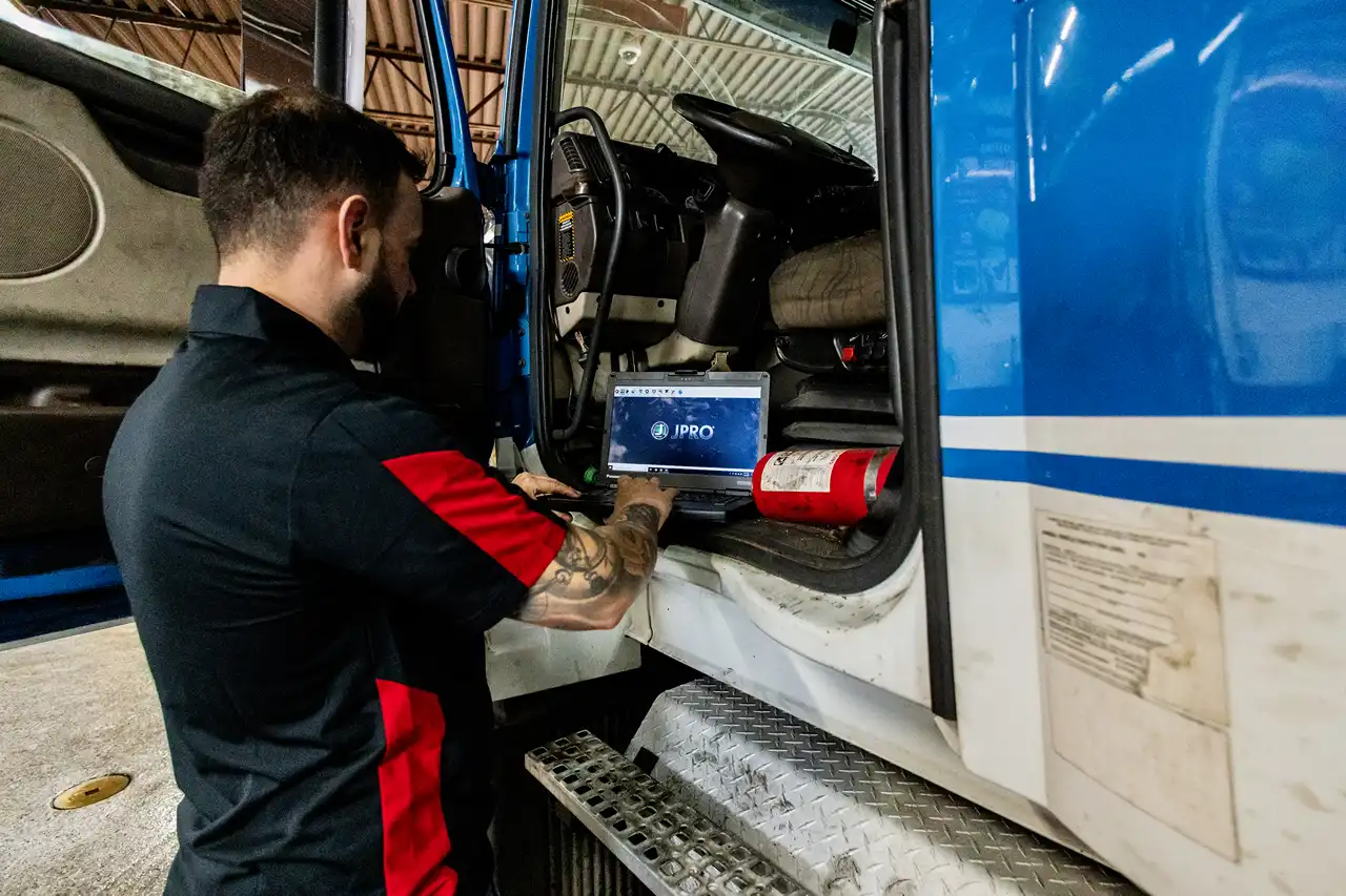 Diagnostic scan: technician uses JPRO laptop plugged into blue semi cab, logging fault codes next to fire extinguisher