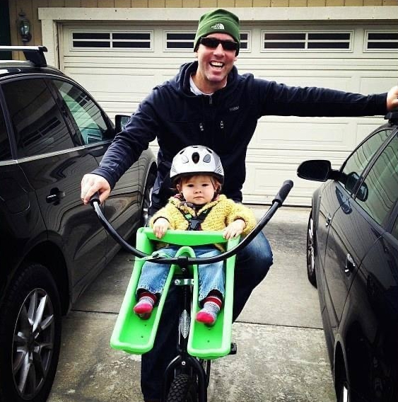 Man and toddler on bike in driveway.
