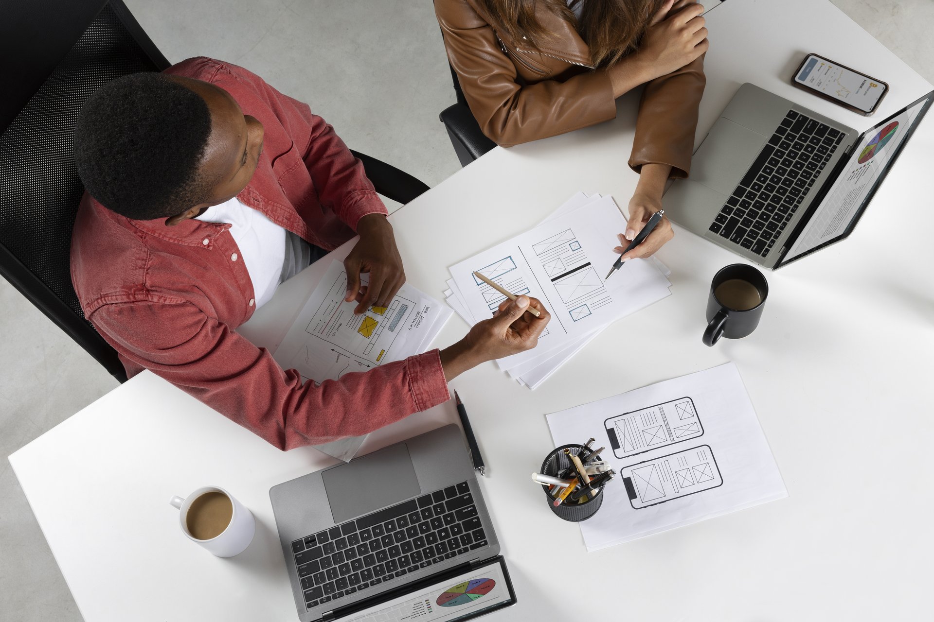 Two people in front of two laptops and two coffees working on charts