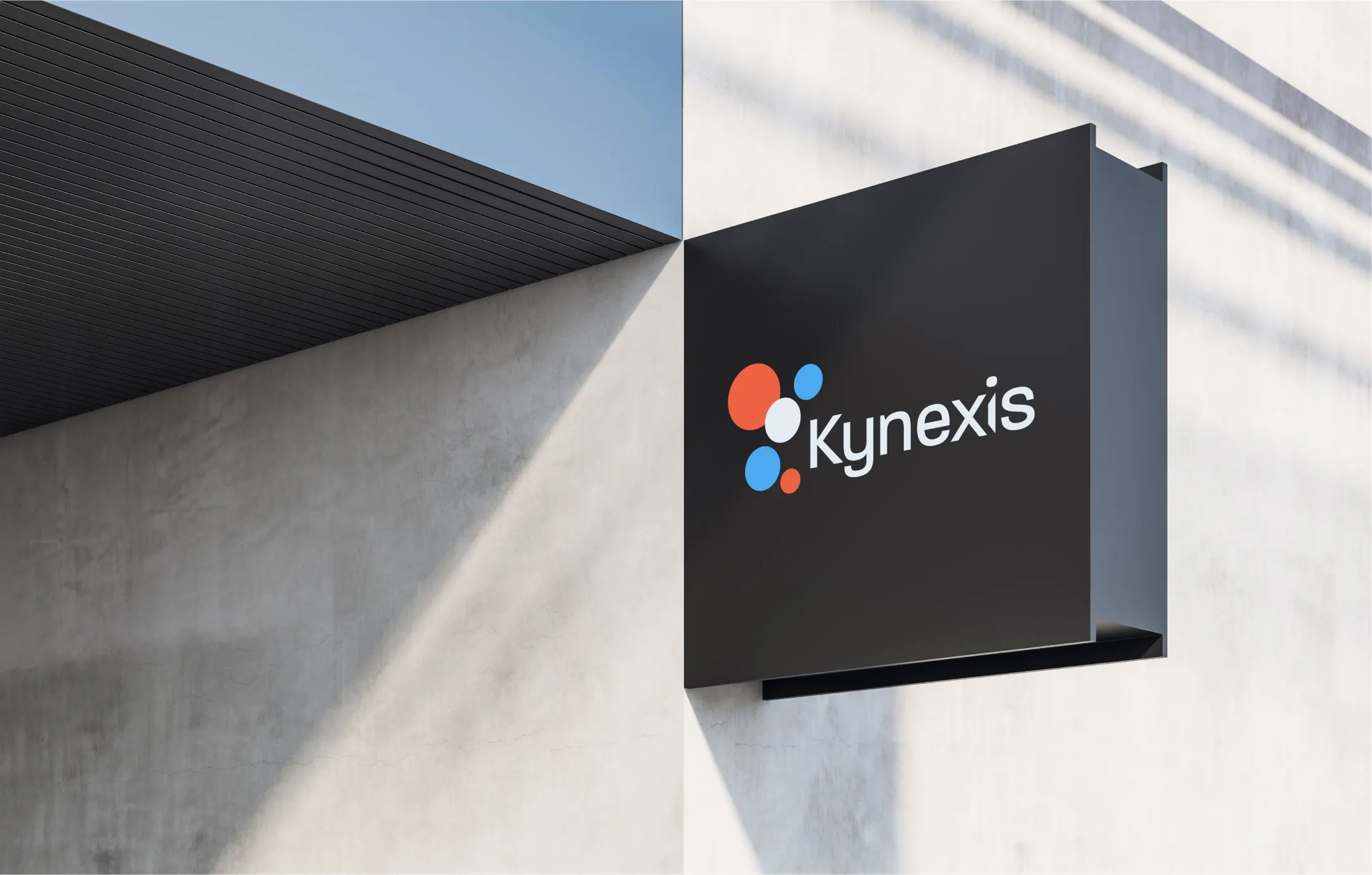 Black rectangular sign mounted on a light concrete wall displaying the kynexis logo with colorful circular design elements.