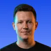 Portrait of a man with short hair wearing a black shirt against a blue gradient background.