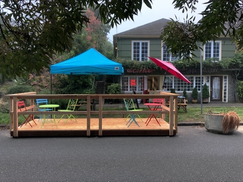 Outdoor seating in front of a cafe, including multi-colored chairs and umbrellas.