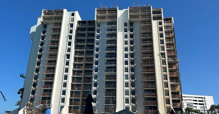 Tall modern building under construction with scaffolding on the facade against a clear blue sky.