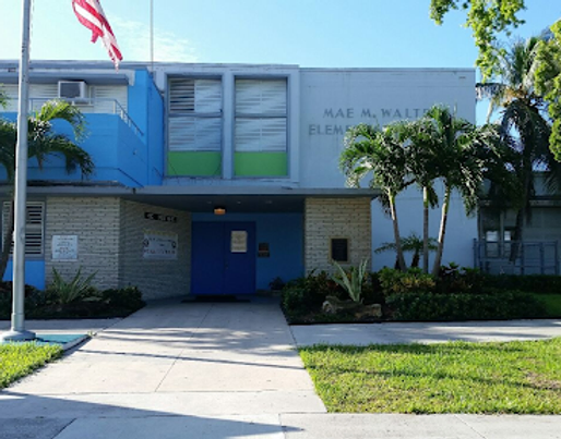 Front entrance of Mae M. Walters Elementary School with blue doors, a flagpole with the American flag, and palm trees flanking the walkway.