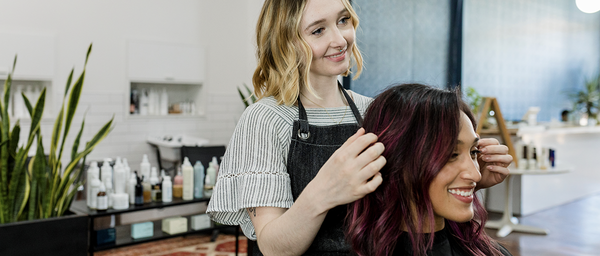 Stylist showing a smiling client her hair beside a salon retail shelf, illustrating Q2 product trends for online store sales