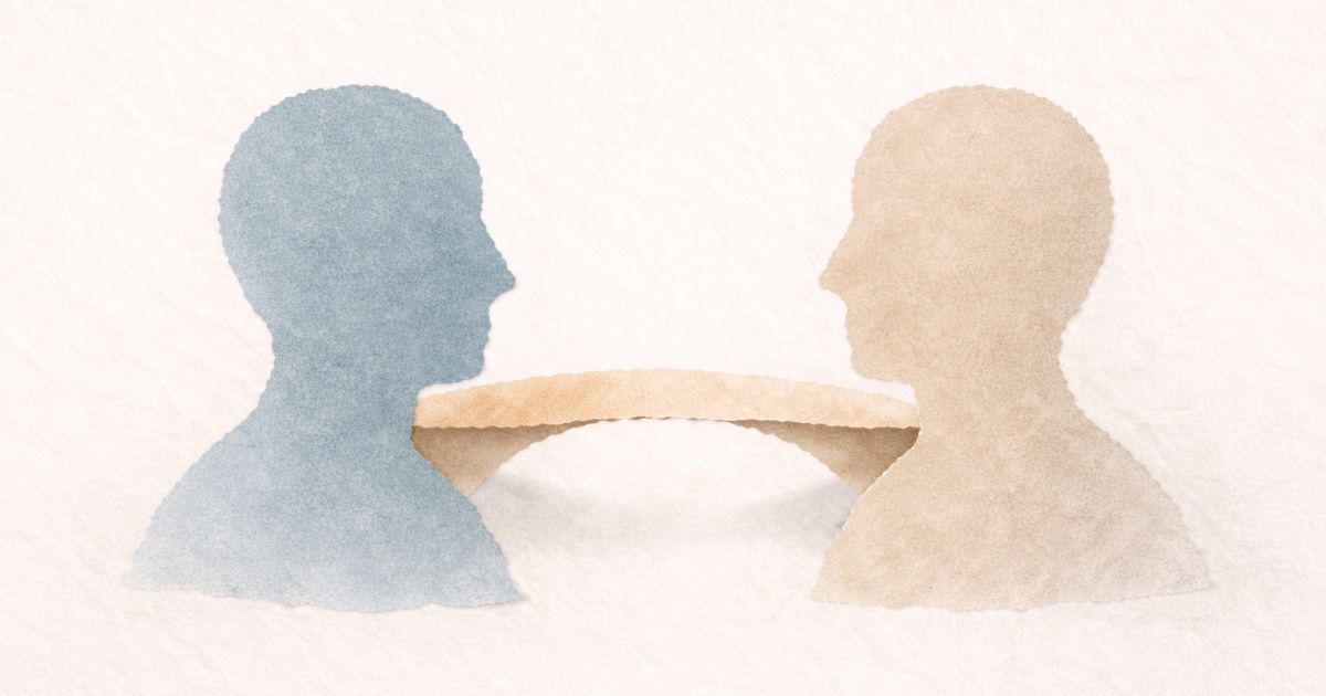 Two abstract torn-paper silhouettes in muted blue and soft beige face one another across a small gap. A simple torn-paper bridge gently connects them at chest level, slightly lifted from the textured cream background, symbolising empathy as a deliberate connection between perspectives.