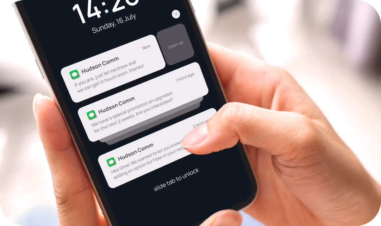 Close-up of a hand holding a smartphone showing three text notifications from Hudson Comm on the lock screen dated Sunday, 16 July.