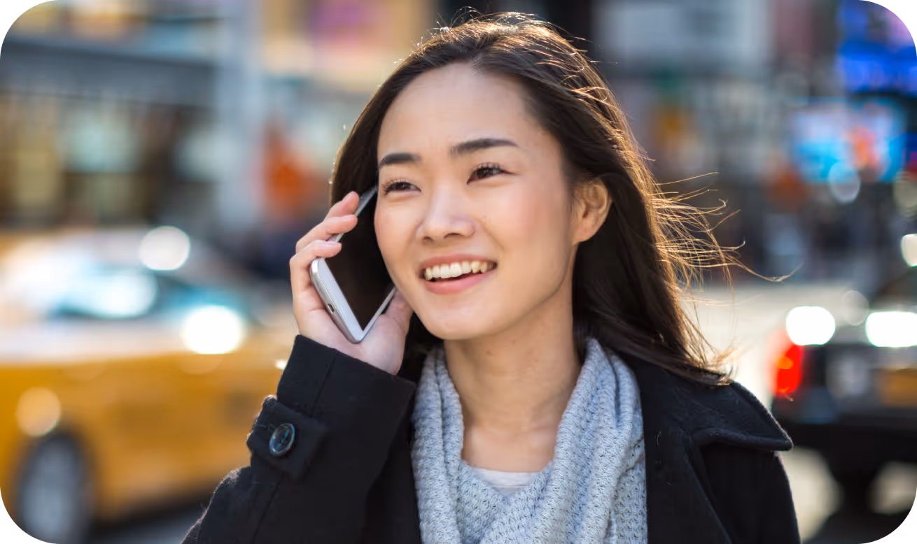 Smiling woman with long dark hair talking on a smartphone outdoors in a city street.