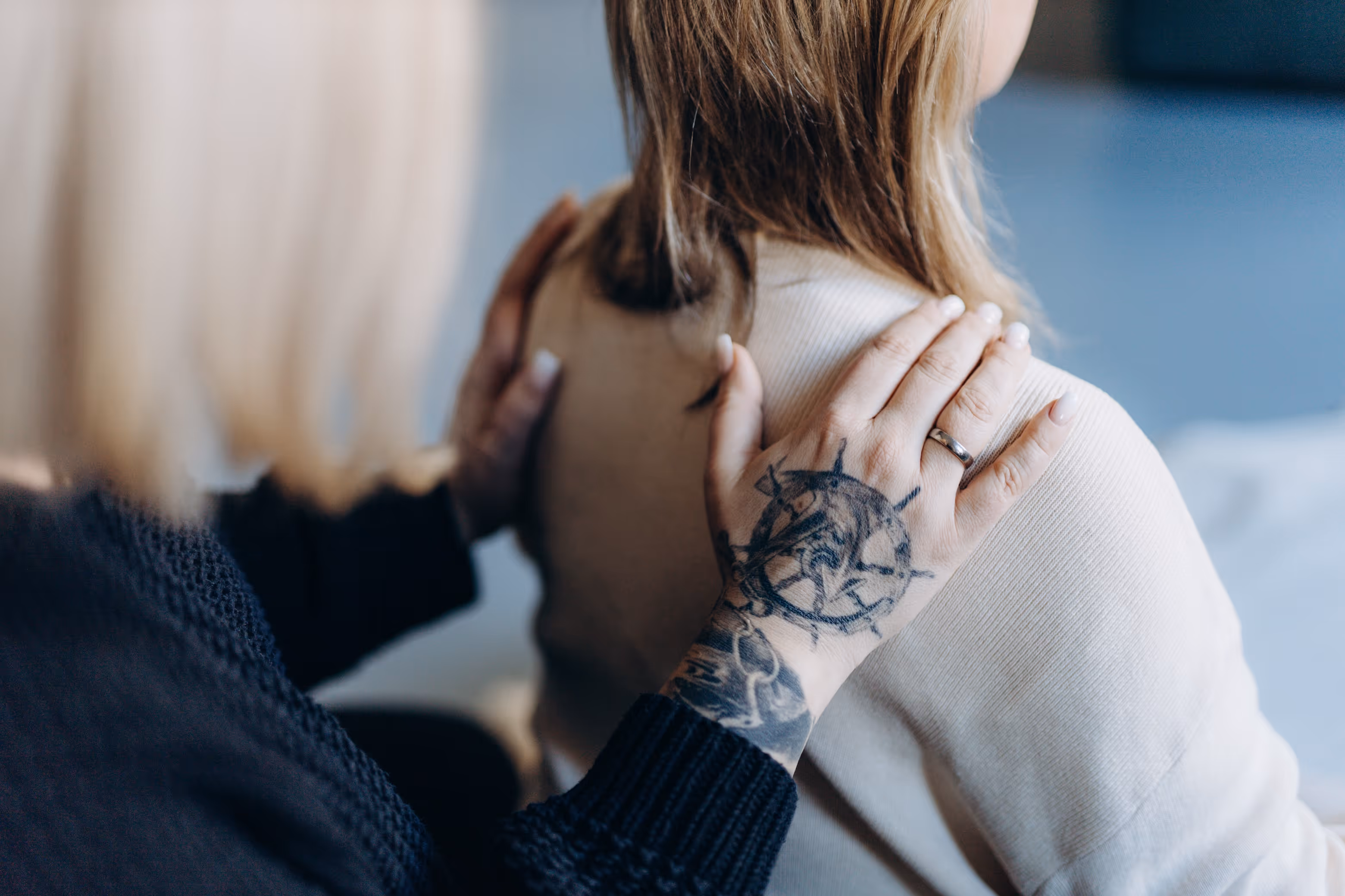 Annika Fischer, die sanft von hinten die Hände auf die Schultern einer anderen Person legt.