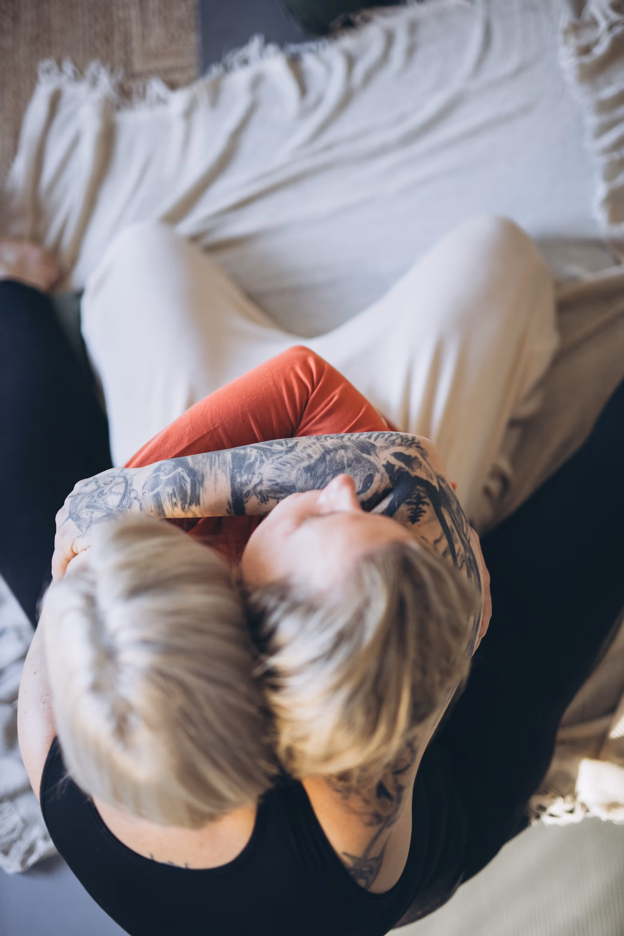 Blick von oben auf zwei Menschen, die sich umarmen, während sie auf einer hellen Decke sitzen.