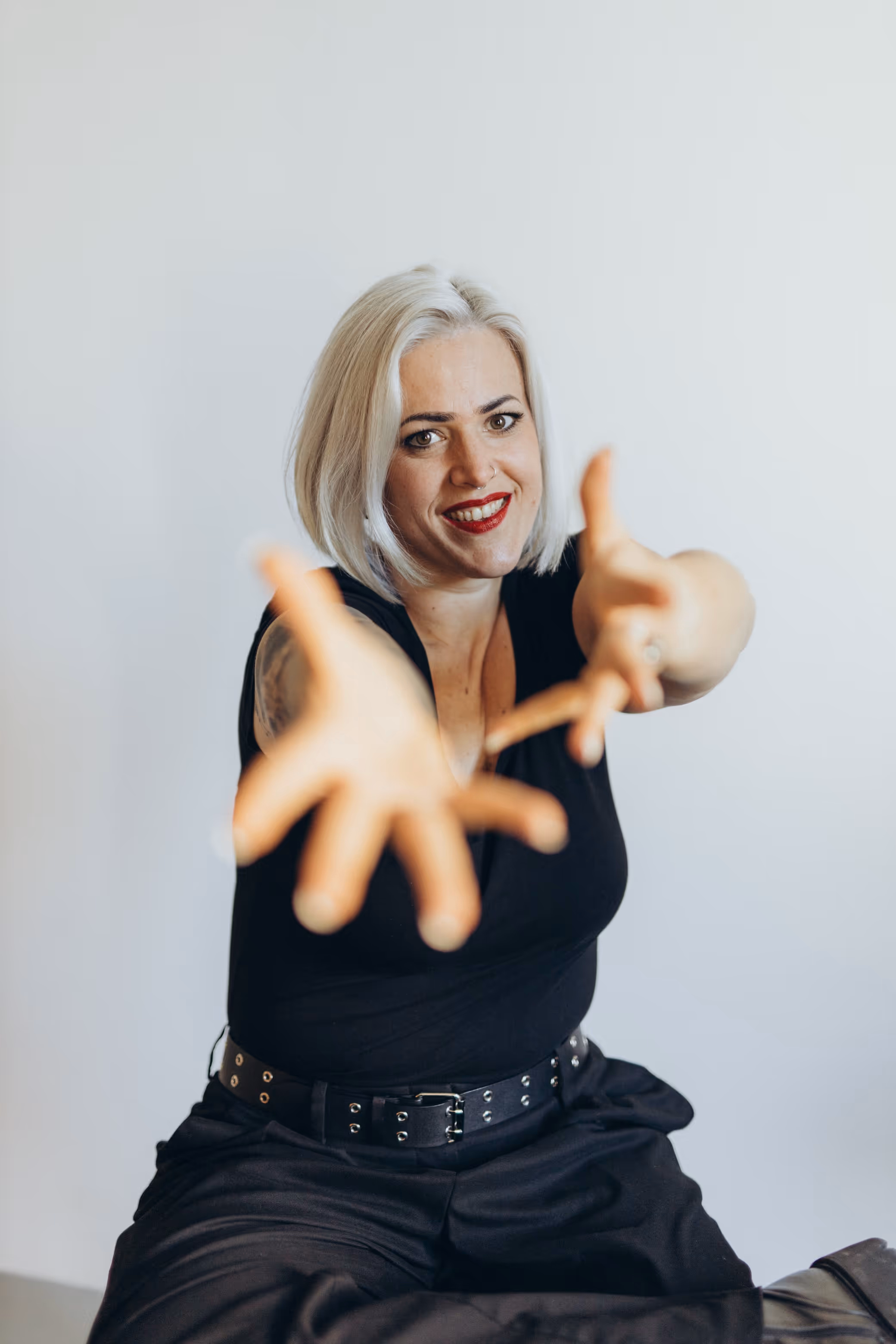 Lächelnde Annika Fischer mit kurzen blonden Haaren, die in schwarzer Kleidung und mit einem Gürtel bekleidet ist und ihre Hand in Richtung Kamera ausstreckt.