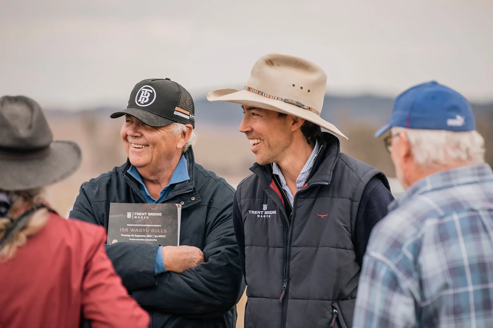 Wal and Charlie Perry from Trent Bridge Wagyu are standing shoulder to shoulder, smiling and looking off into the distance, Wal is holding a Trent Bridge Wagyu sale catalogue in his arms which are folded across his chest. 