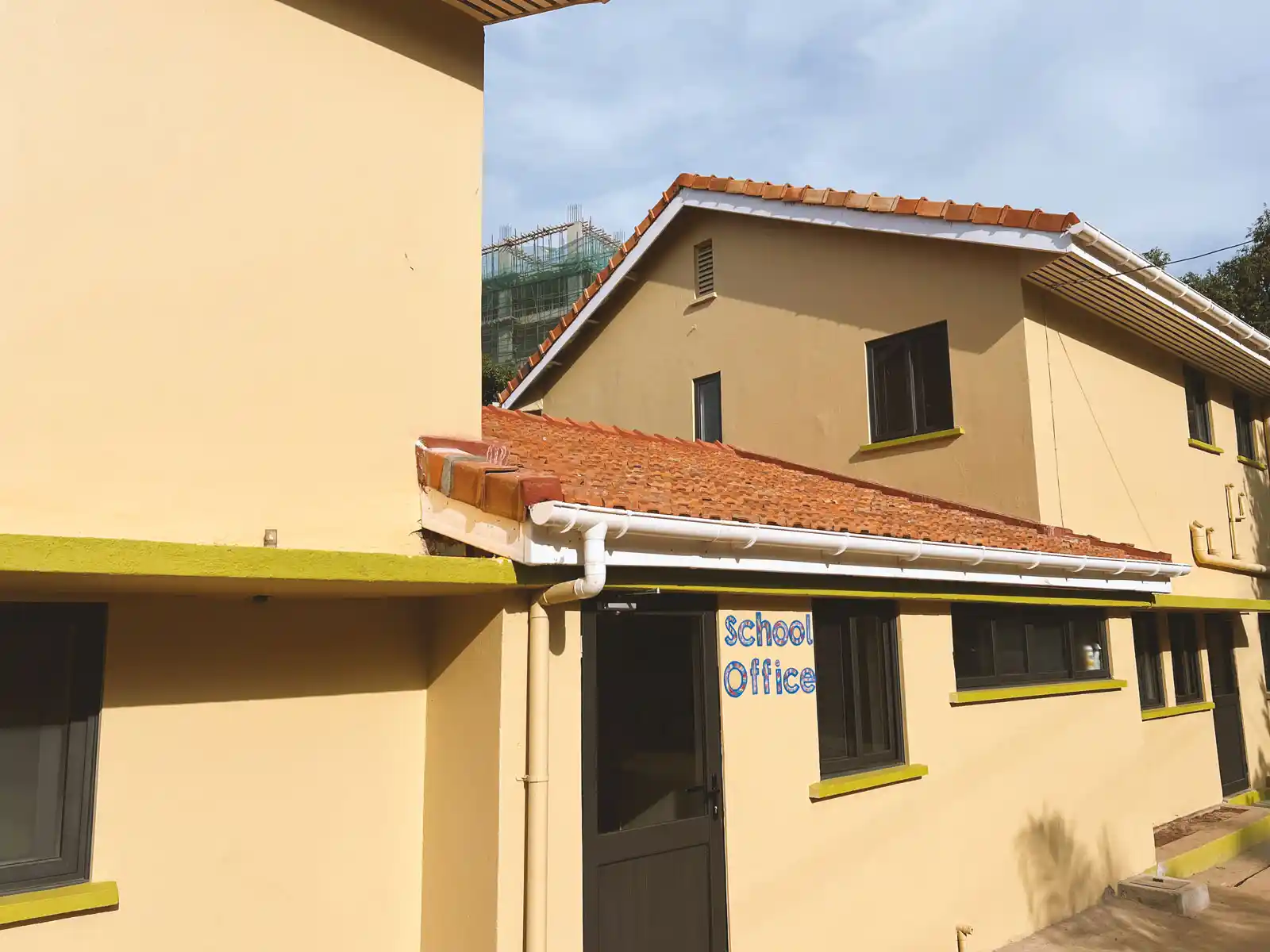 Yellow school building with red tiled roofs and dark windows under a clear sky, with a door labeled 'School Office'. The Ark Preschool Kampala Uganda.