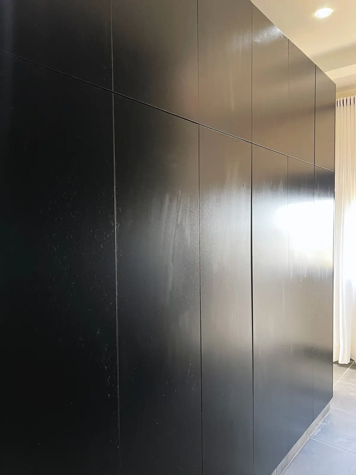 Glossy black wall-panel cabinets with subtle reflections next to a window with white curtains. Busalaba Residential Remodel in Kampala by Elevate Holdings Limited.