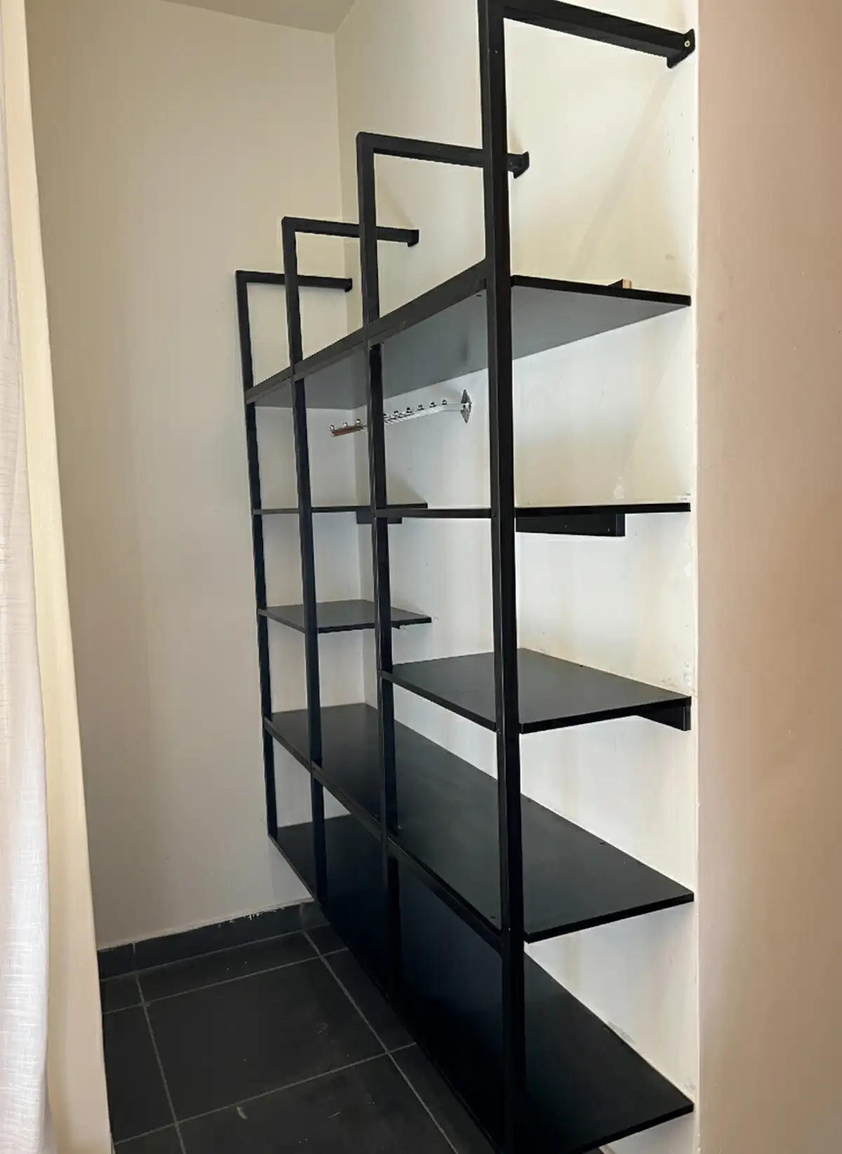 Empty black metal shelving unit mounted against a white wall in a small tiled room. Busalaba Residential Remodel in Kampala by Elevate Holdings Limited.