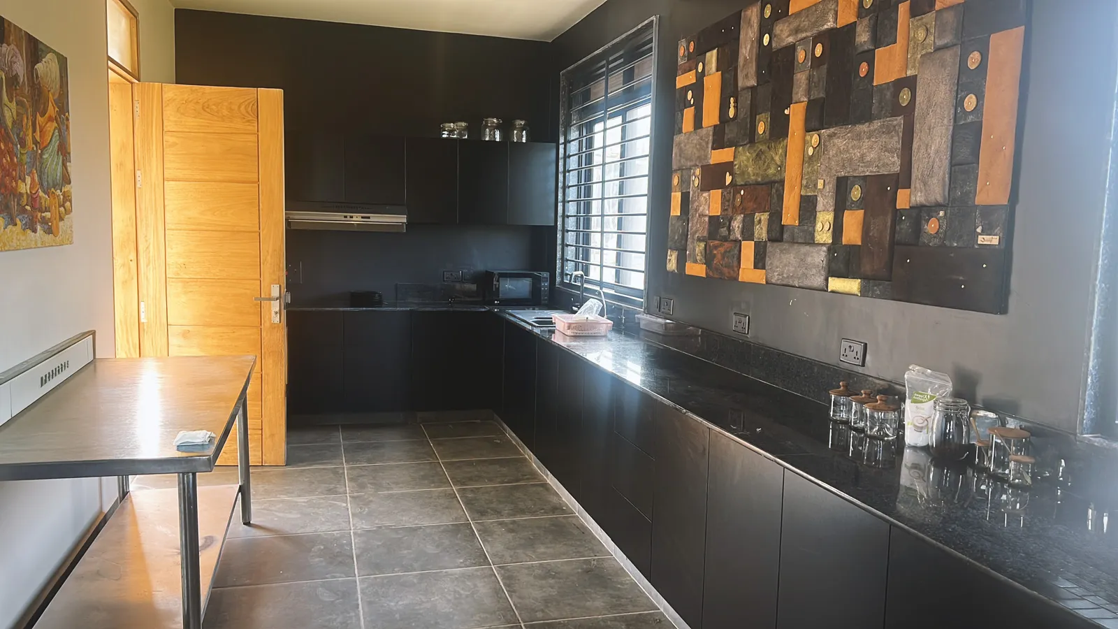 Modern kitchen with black cabinets, black granite countertops, decorative wall art, and large window with metal bars.