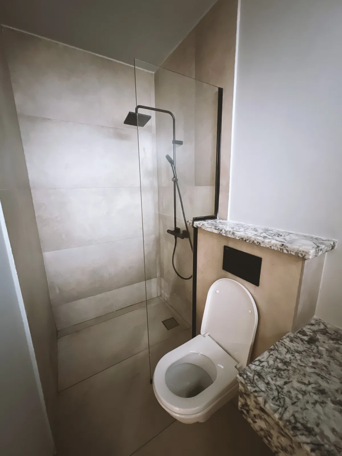 Modern bathroom with white toilet next to a walk-in shower enclosed by a glass panel and marble countertops. Sonde Residential Remodel by Elevate Holdings Limited.
