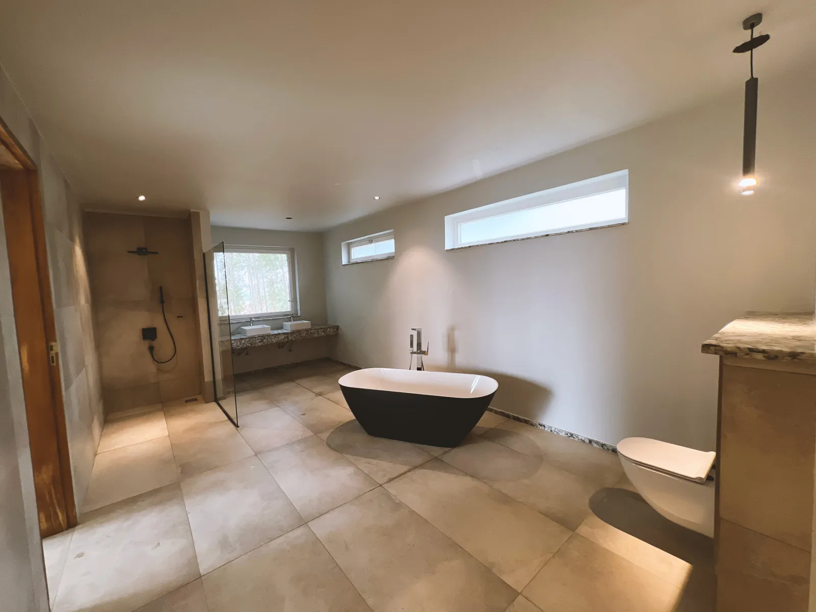 Spacious modern bathroom with a freestanding black and white bathtub, walk-in shower with glass door, double sink vanity, and a wall-mounted toilet. Sonde Residential Remodel by Elevate Holdings Limited.