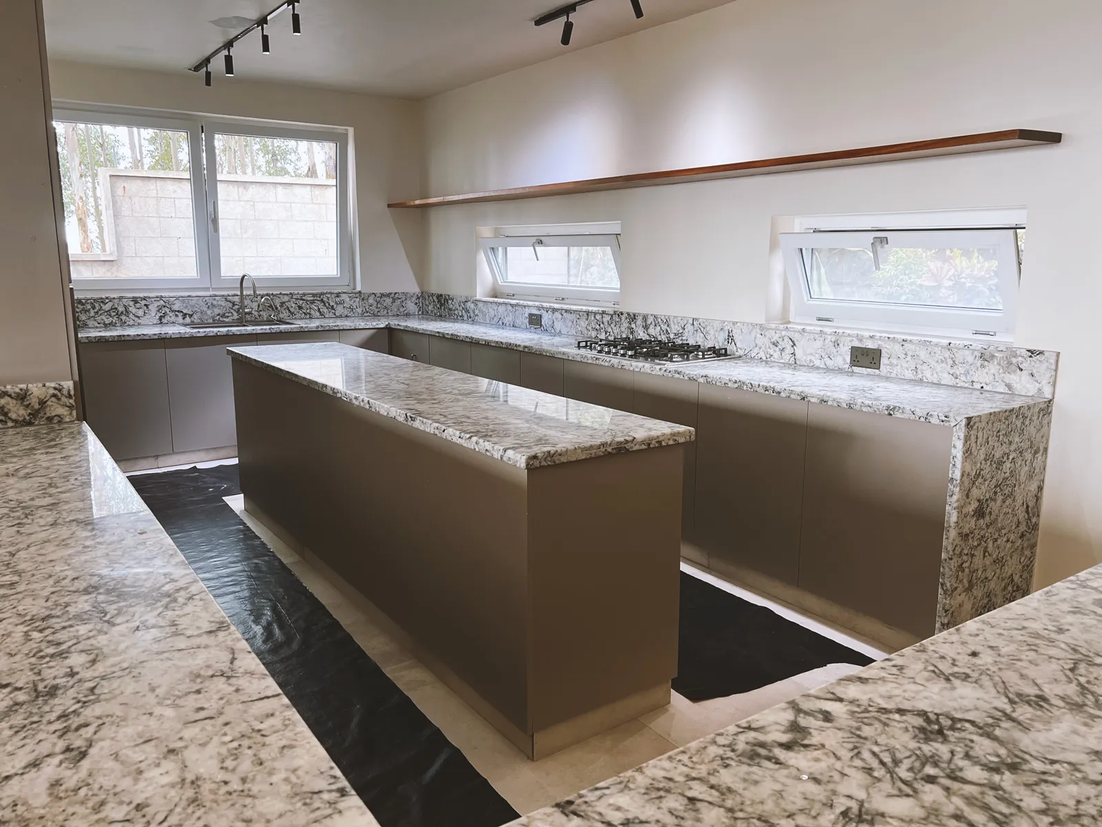 Modern kitchen with marble countertops, a central island, gas stove, and two angled windows above the counters. Sonde Residential Remodel by Elevate Holdings Limited.