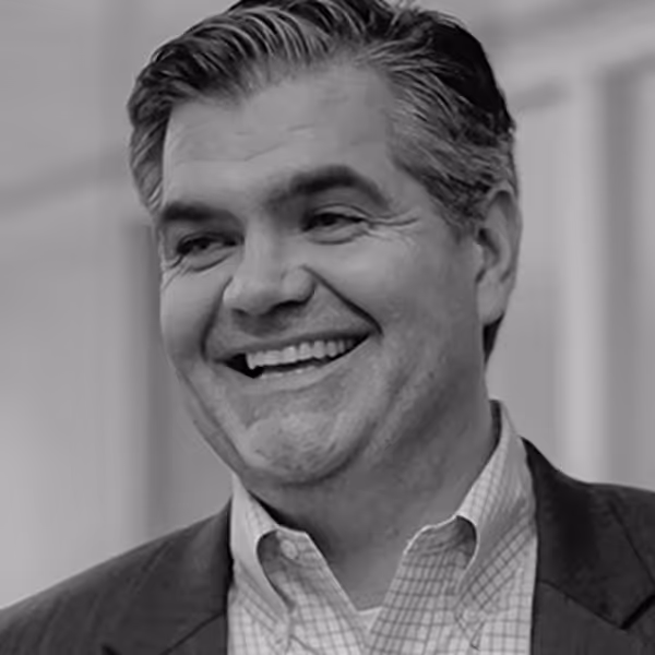 Smiling middle-aged man with neatly combed hair wearing a checkered shirt and blazer.