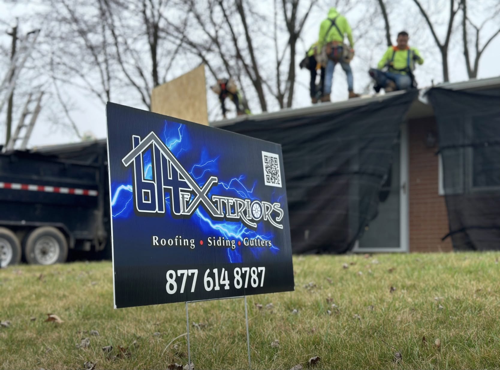 614 Exteriors roofing crew working on a Columbus, Ohio home with company yard sign in the foreground